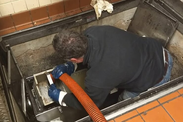 A technician cleaning a grease trap in a commercial kitchen