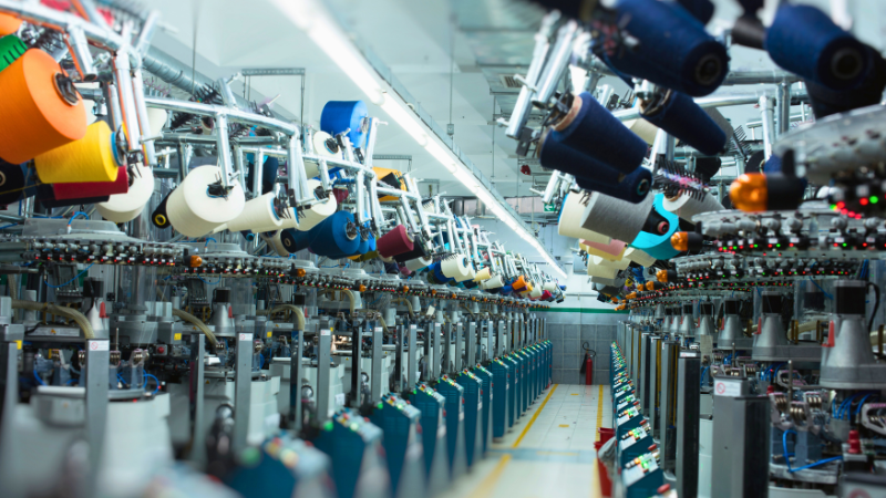 Rows of automated textile machinery with spools of colored yarn in a factory setting.