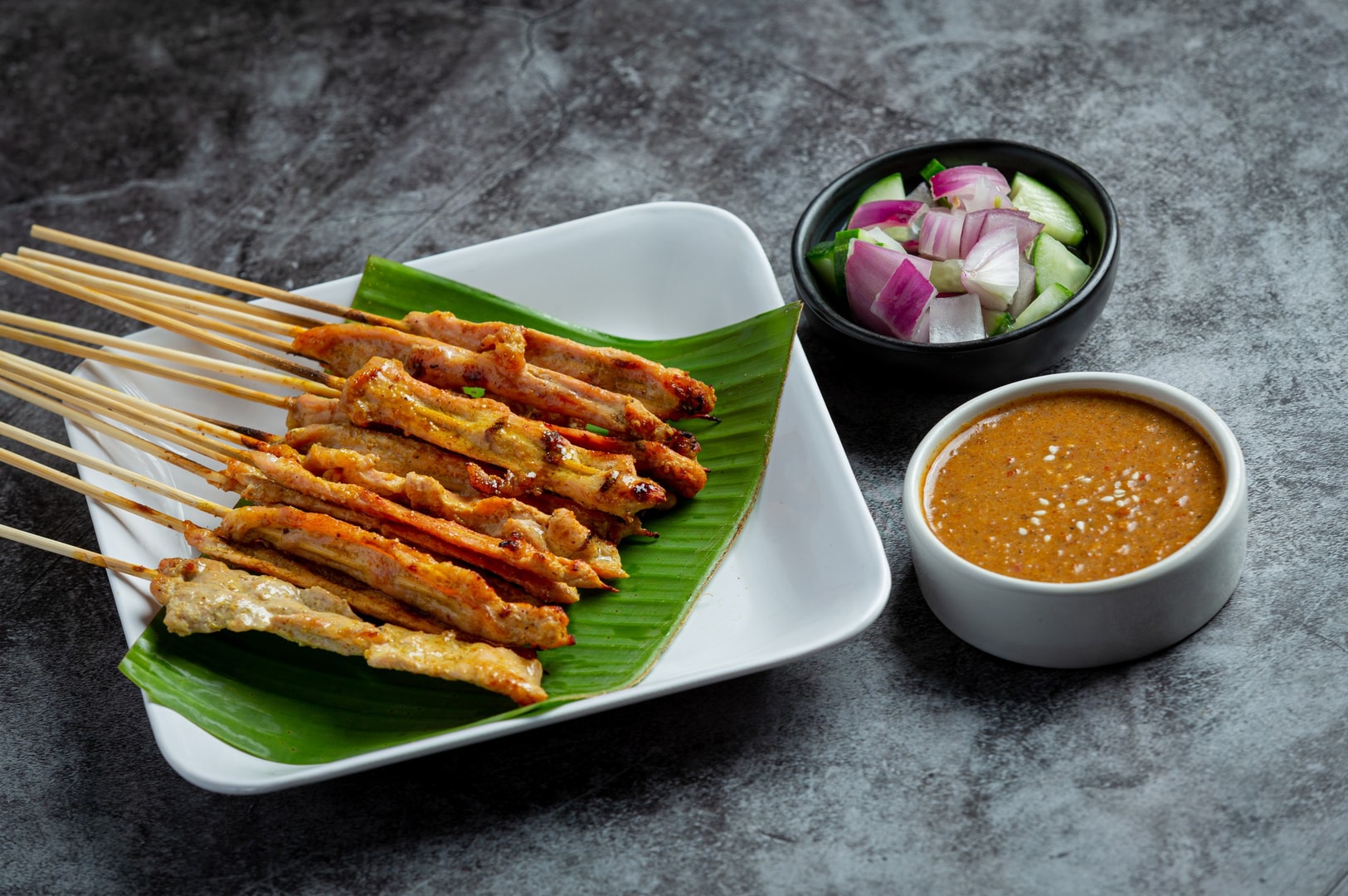 A plate of Thai satay chicken skewers accompanied by a dipping sauce for added flavor.