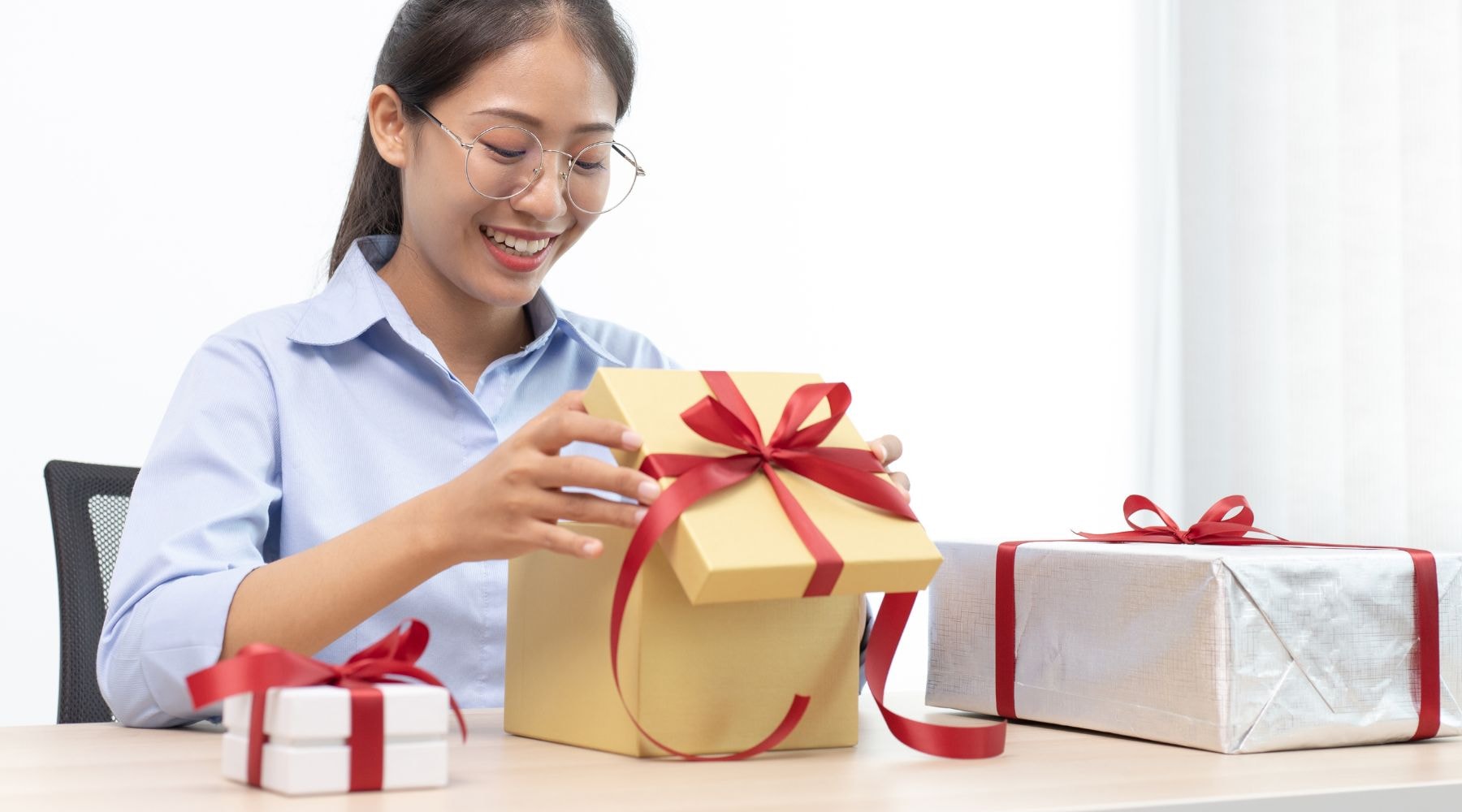 Excited young woman opening a large yellow gift box at her office desk.