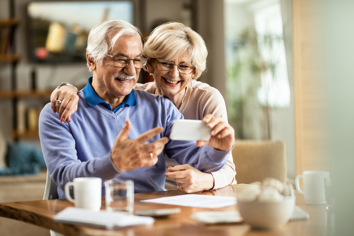 Mature couple with glasses and white hair having coffee and smiling at their cell phone. 