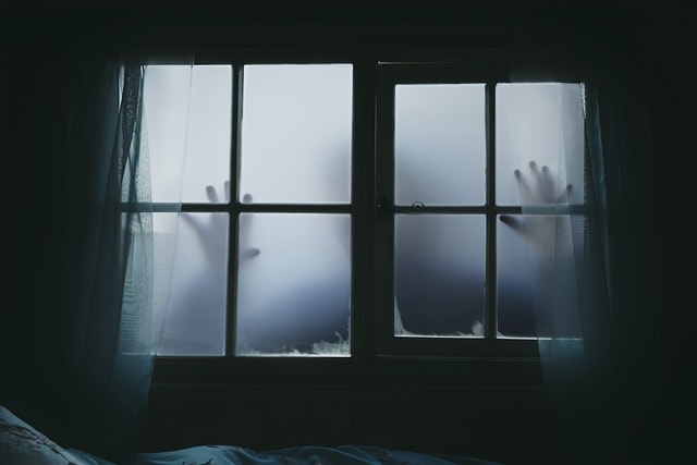 A person outside a creepy window representing horror tropes of suspense.