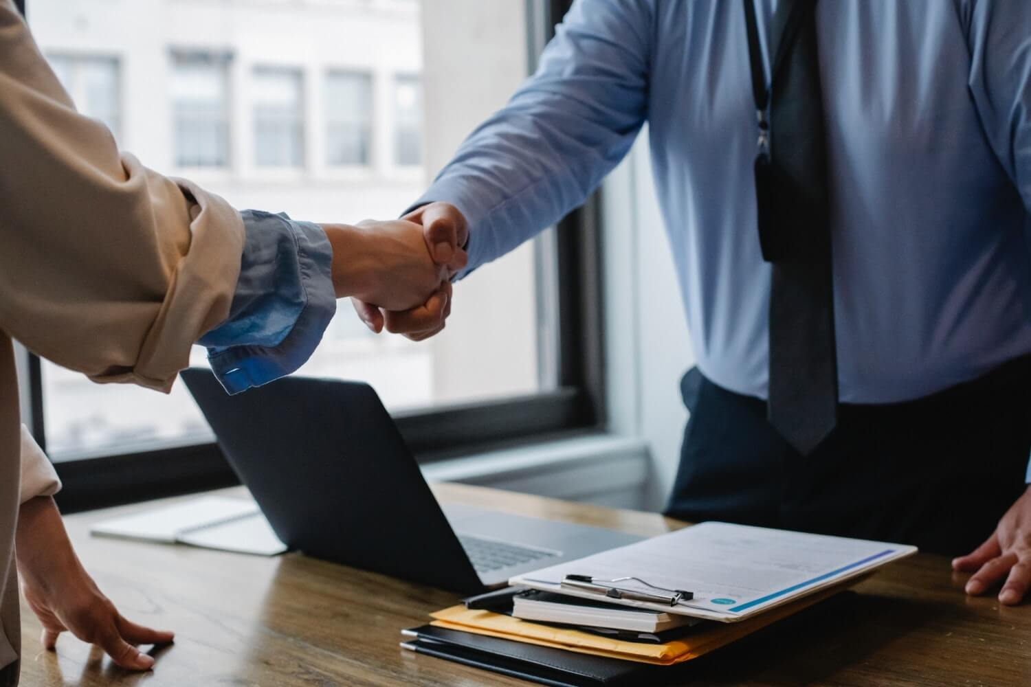 two people shaking hands over a desk after an exit interview at a small business