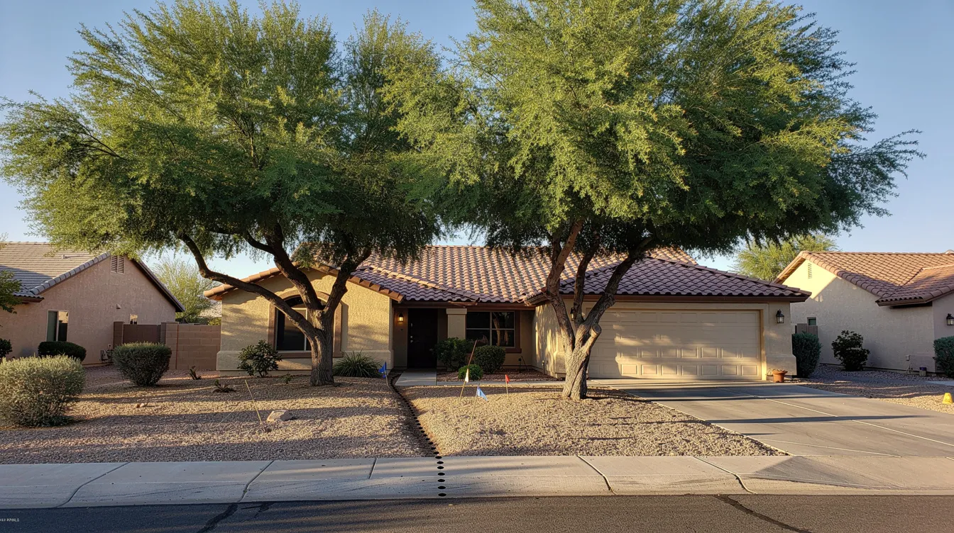The image depicts a residential home in the Phoenix area, featuring large mature trees in the front yard, with the sewer line path visible nearby. This setting highlights the potential impact of tree roots on sewer pipes, emphasizing the importance of methods like hydro jetting for effective drain cleaning and maintaining the plumbing system.