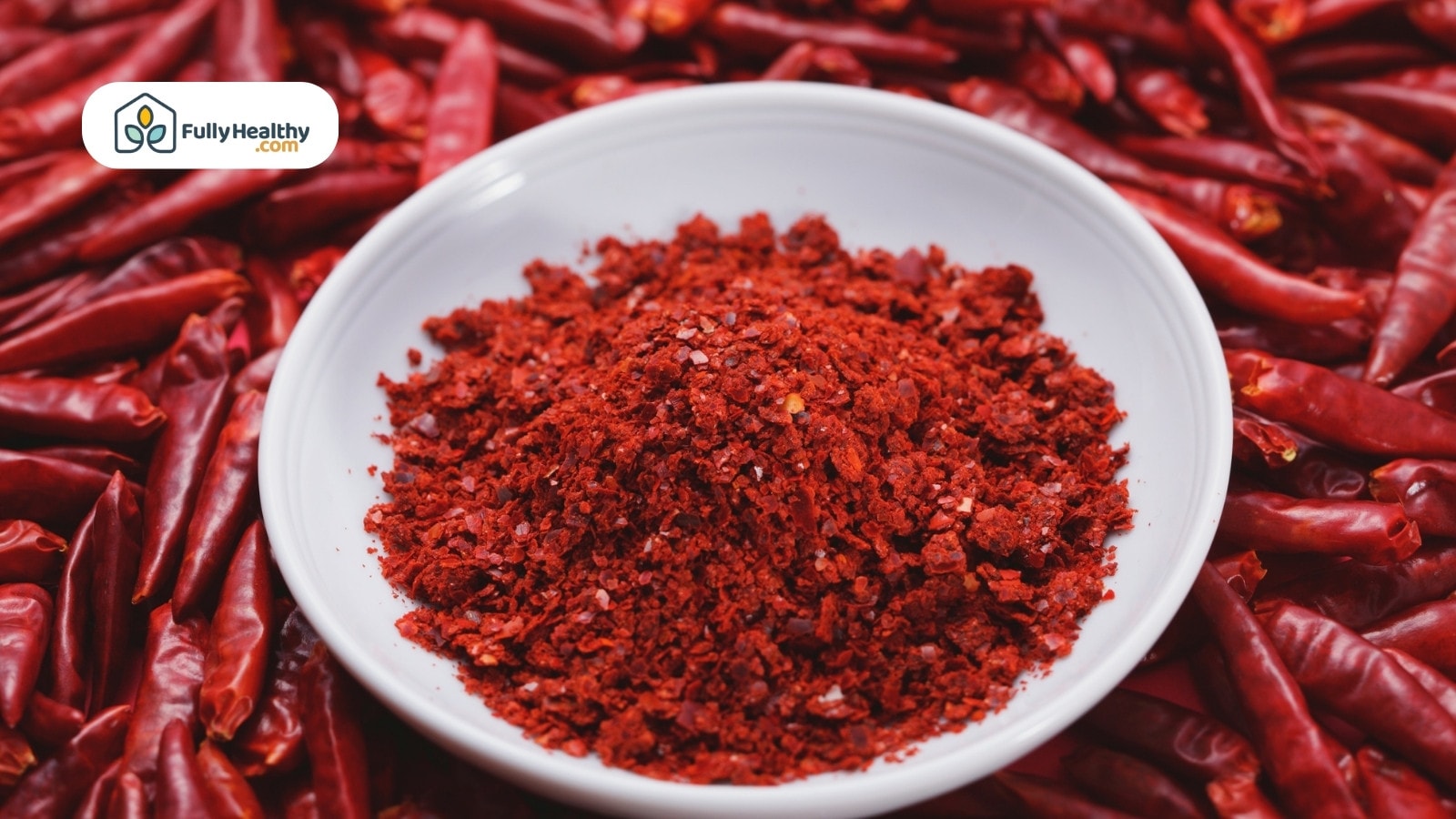 Bowl of crushed red chili flakes on dried chili background