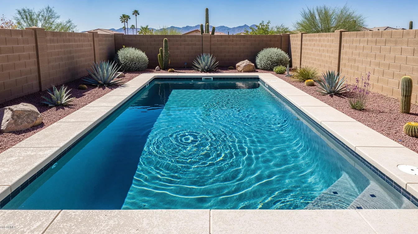 A residential swimming pool with sparkling clear blue water is situated in a Phoenix backyard, surrounded by desert landscaping and a sturdy block wall. This serene setting highlights the importance of leak detection services to prevent pool leaks and save on water bills in Arizona.