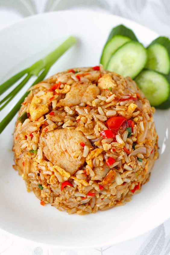 Thai fried rice served in a white bowl garnished with fresh herbs, chicken and vegetables.