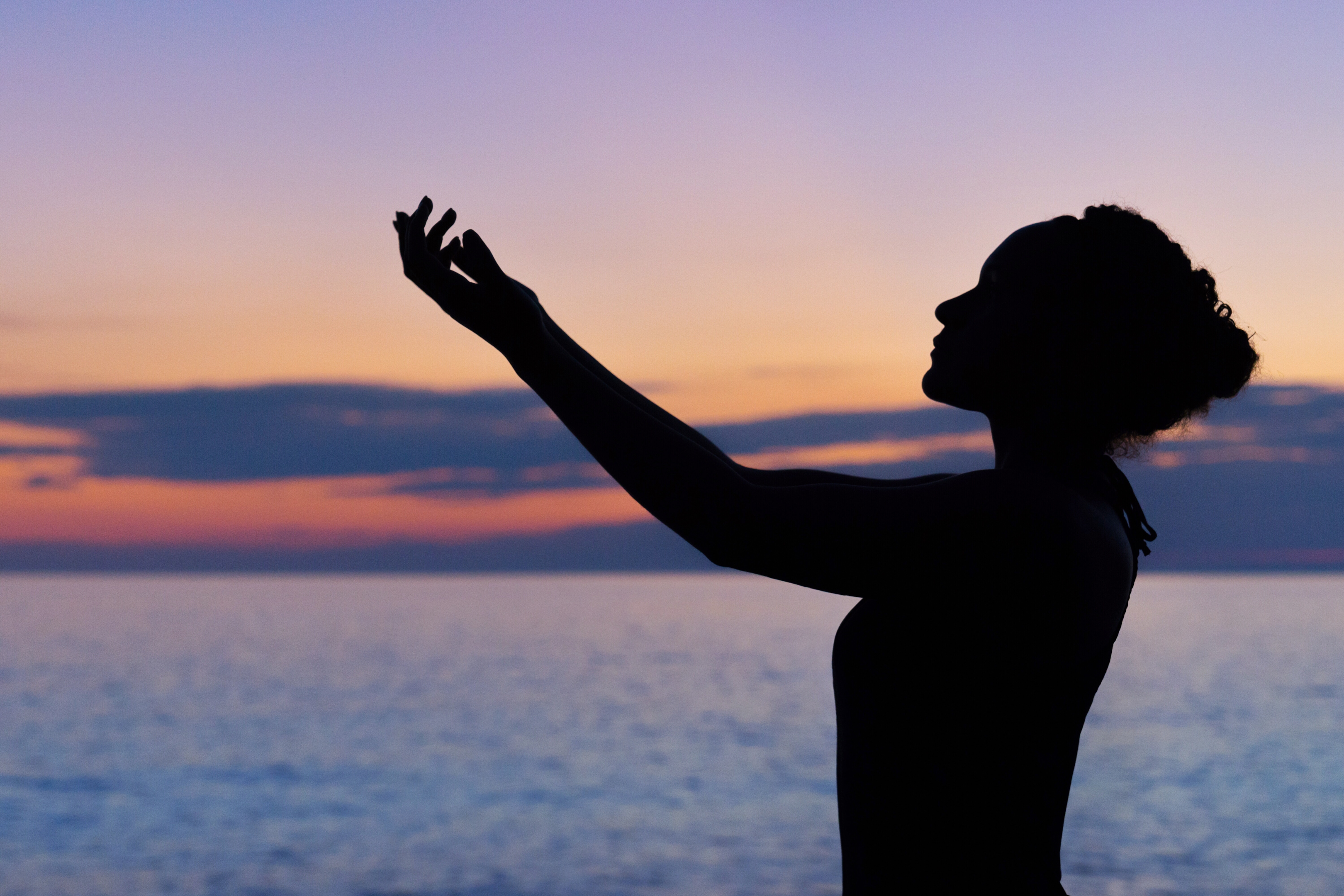 silhouette of a woman with her hand outstretched before the sea at sunset