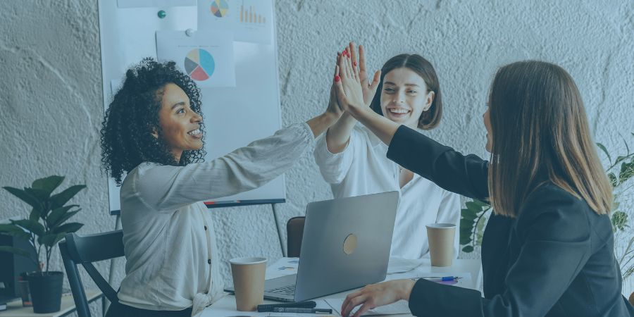 Women doing remote work sitting at a table and giving a high five