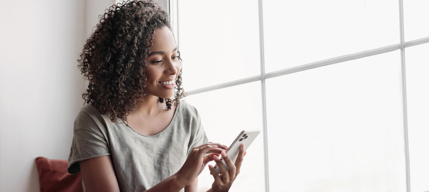 Happy young woman sitting by a window and checking her email.