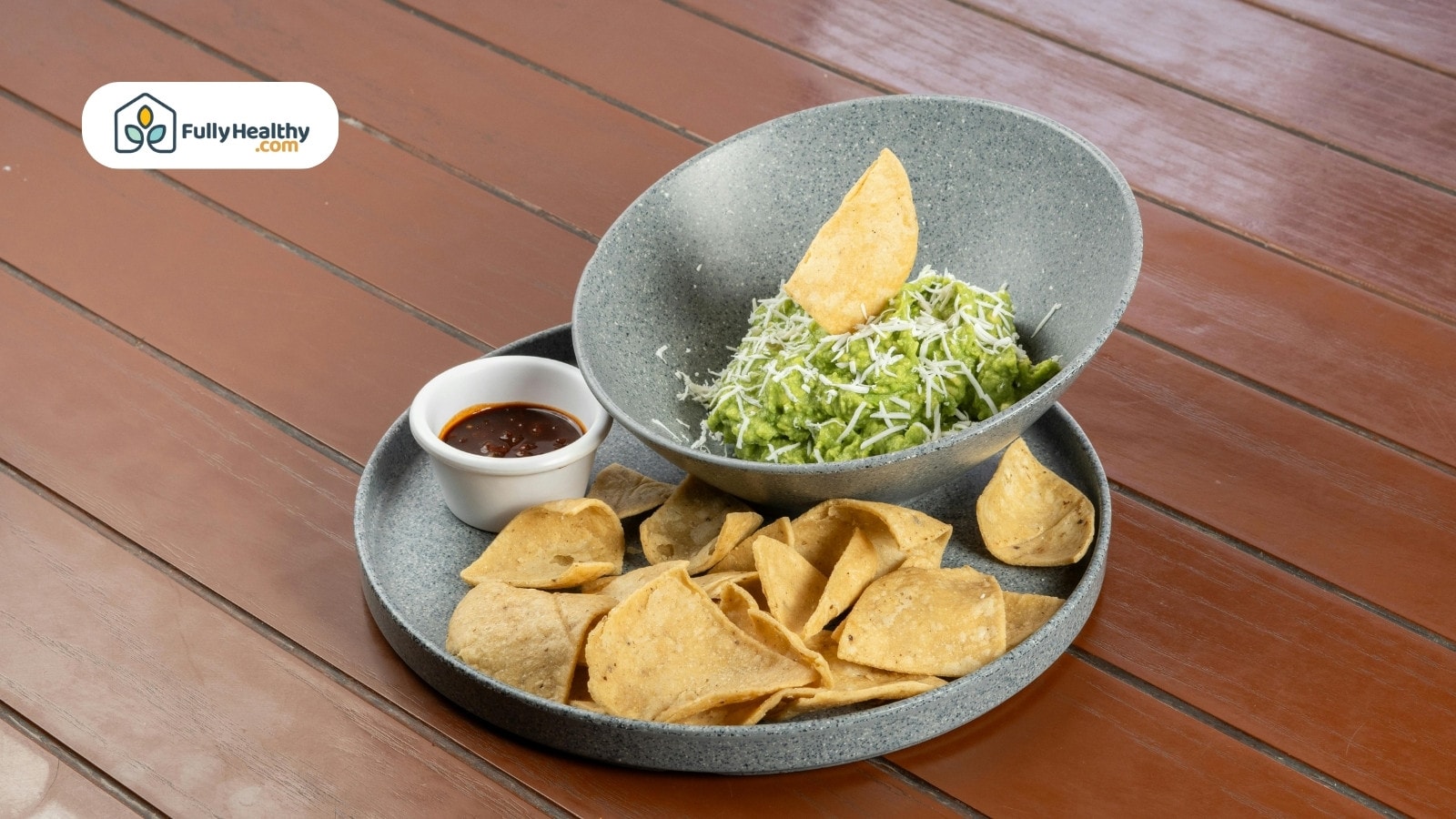 Guacamole with tortilla chips and salsa in a gray bowl.