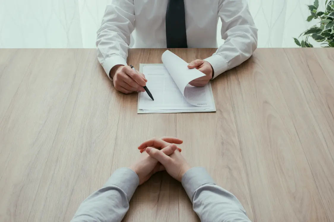 Close-up of broker presenting contract papers to a client across the table, highlighting the outcomes of asking the right interview questions for business brokers.