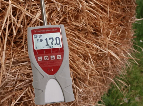 A hay moisture tester with a probe inserted into a bale of hay