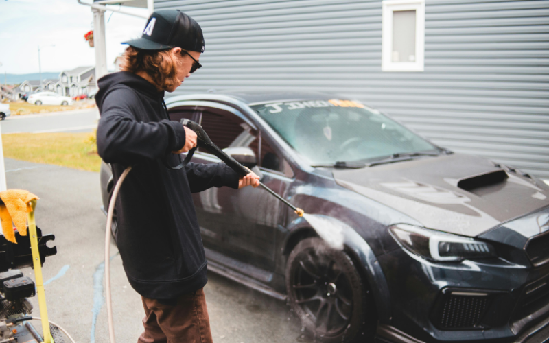 Person using a pressure washer to rinse a black car during car washing