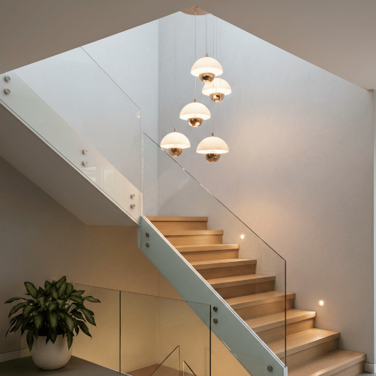 Cluster of modern white dome pendant lights hanging above a staircase with glass railing and warm ambient lighting.