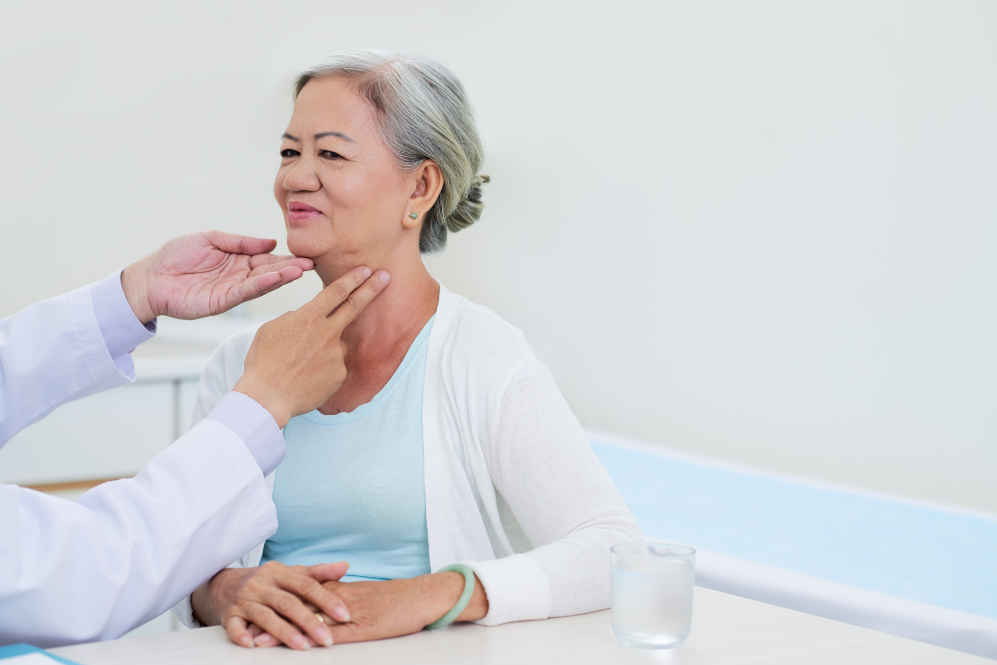 An image of a doctor's hands feeling a female patient's throat for tightness. 