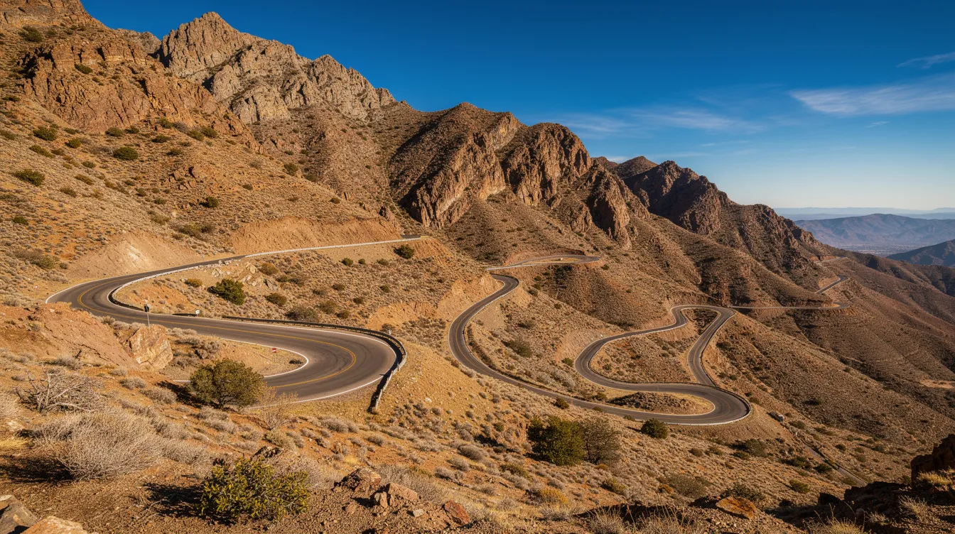 Une voiture sur une route de montagne en lacets entre des reliefs arides sous un ciel bleu.