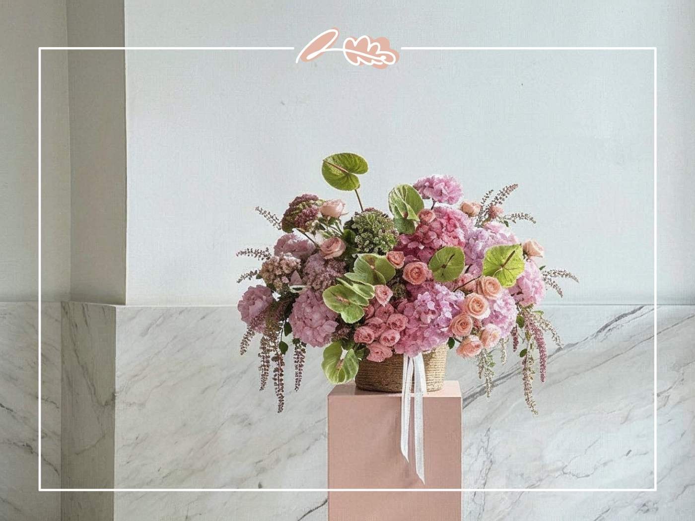 Pink hydrangea arrangement with peach roses, green anthuriums, and trailing amaranthus in a woven basket on a marble backdrop