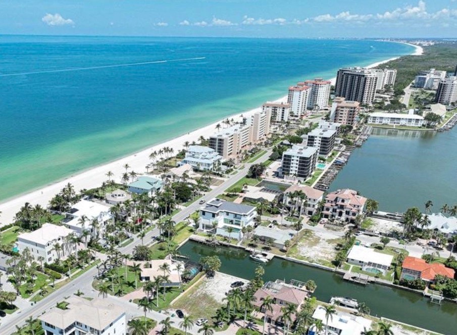 The image depicts luxurious beachfront condominiums at Vanderbilt Beach, showcasing breathtaking panoramic views of the pristine Gulf waters and white sand beach. These exquisite turnkey beachfront properties feature spacious floor plans, floor-to-ceiling windows, and direct beach access, embodying a refined living experience in Naples, FL 34108.
