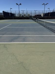 Cracked tennis court with visible surface damage and wear.