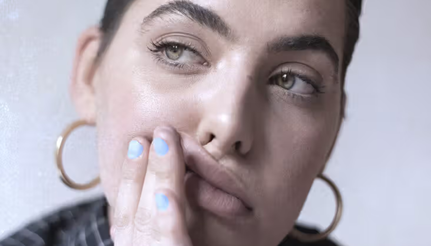 Person som holder hånden mot kinnet og ser bort, som om de kjenner smerte eller ubehag.