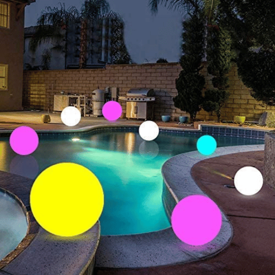 Backyard pool area at dusk, decorated with floating LED globe lights in bright colors like yellow, pink, white, and blue, creating a vibrant and festive atmosphere for outdoor entertaining.