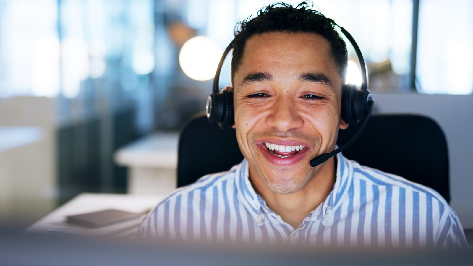 Close-up of a cheerful customer support team representative wearing a headset, smiling while using a computer in a bright office—symbolizing user-friendly cloud PBX features like call routing, voicemail-to-email, and CRM integrations in business VoIP solutions.