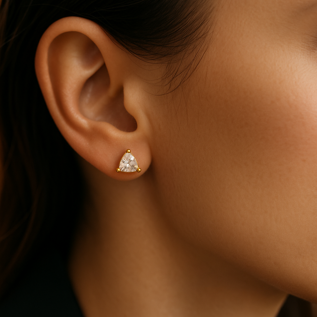 Geltono aukso auskaras su trikampio formos deimantu ant elegantiškos moters ausies.