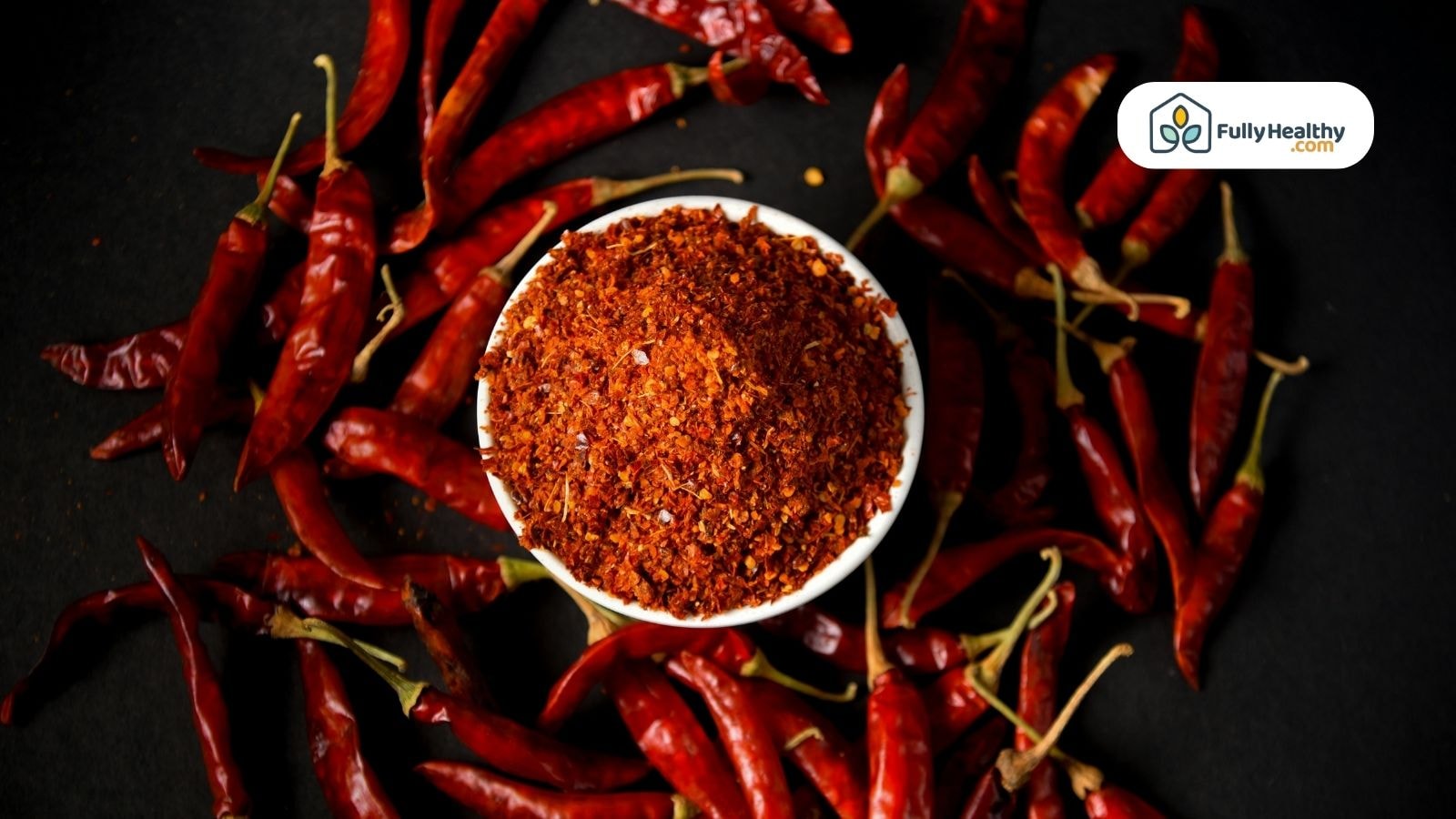 Bowl of crushed Aleppo pepper surrounded by whole dried chiles on black background