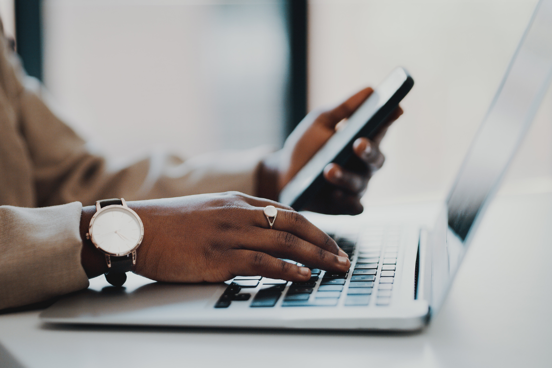 Close-up of a professional using a smartphone and laptop to research business brokers online.
