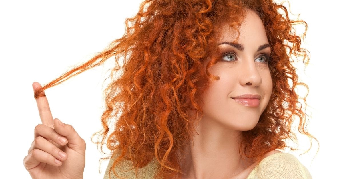 A red-haired woman with curly hair smiles as she plays with her hair, illustrating how to pay excise tax with confidence.