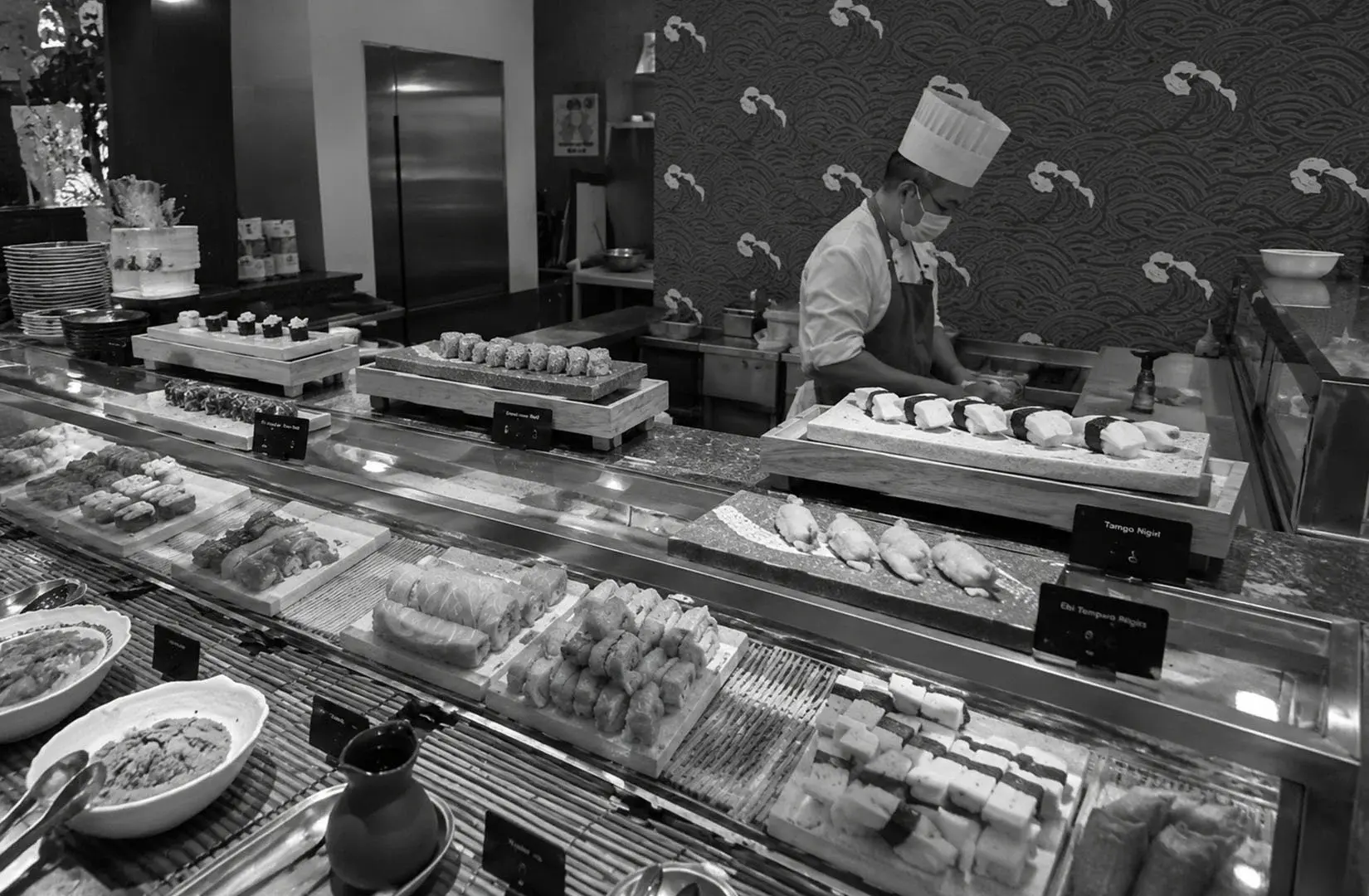 Chef preparing sushi behind a restaurant buffet counter.