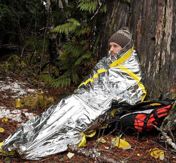 Man wrapped in emergency blanket in forest