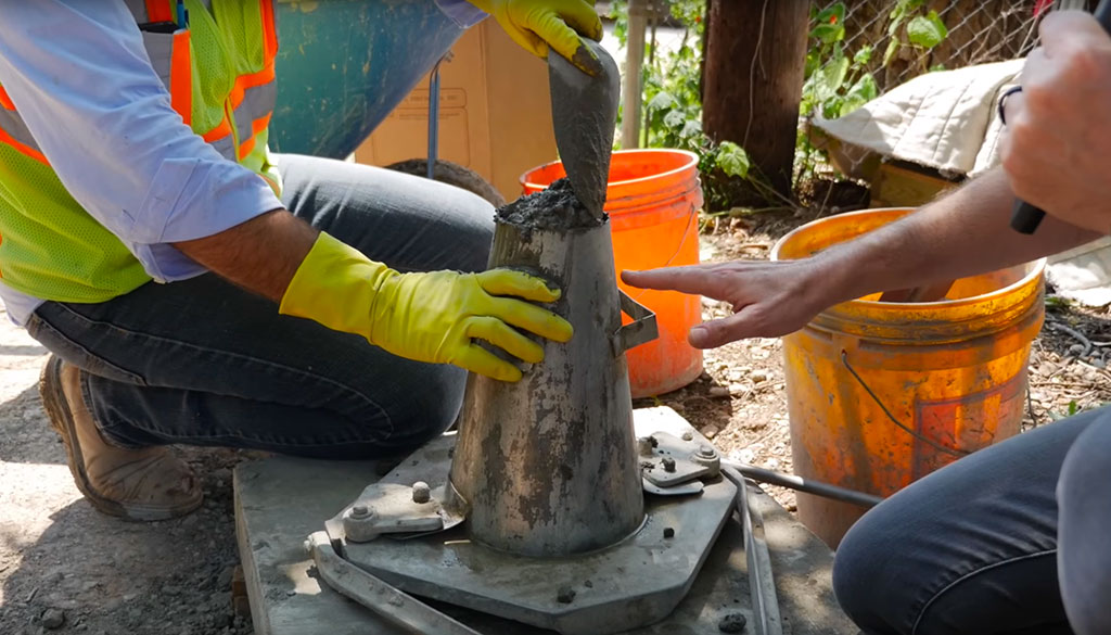 A person holding a slump cone, with a freshly mixed concrete sample inside, ready to perform a slump test