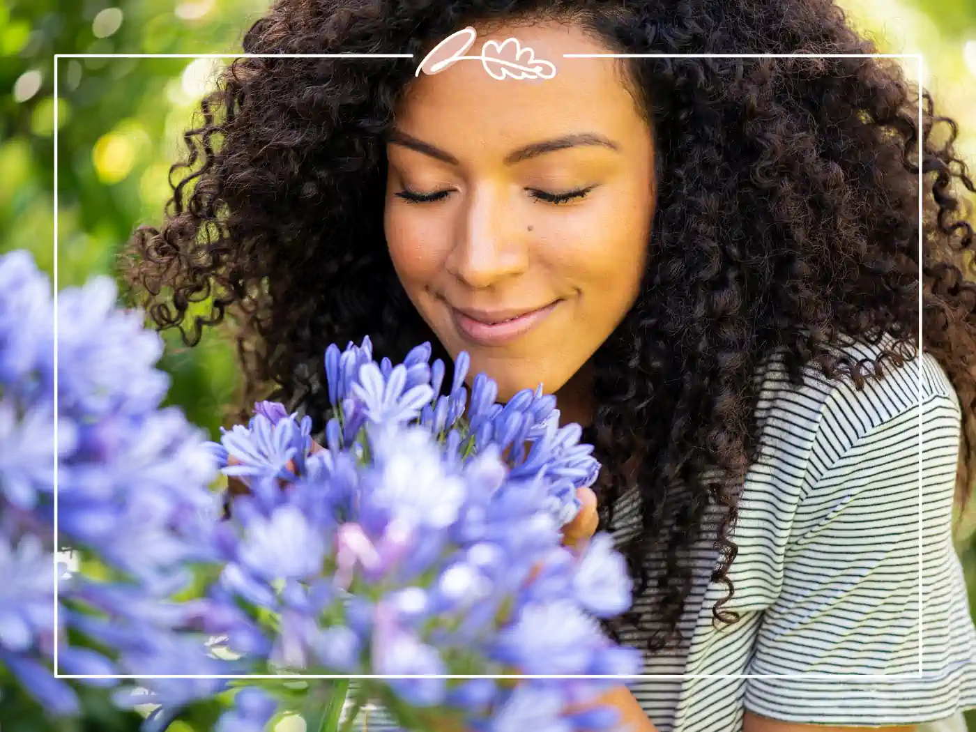 A woman smiling as she inhales the fragrance of beautiful purple flowers in a garden. Fabulous