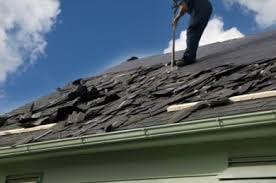 An image of a roofer in the middle of an asphalt shingle replacement on a residential home during the summer against blue skies and white clouds. 