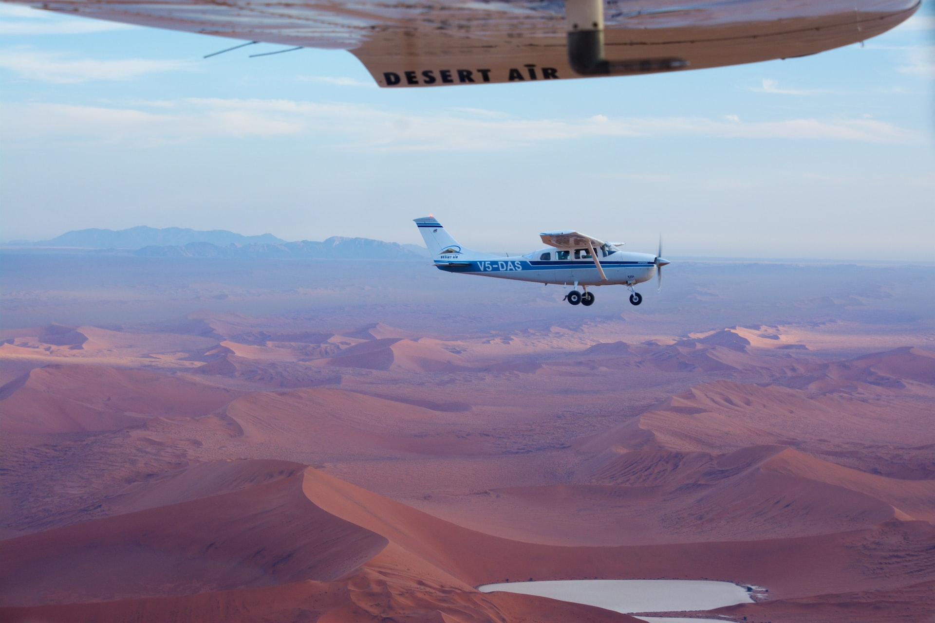 Two small airplanes flying over a desert with an oasis.