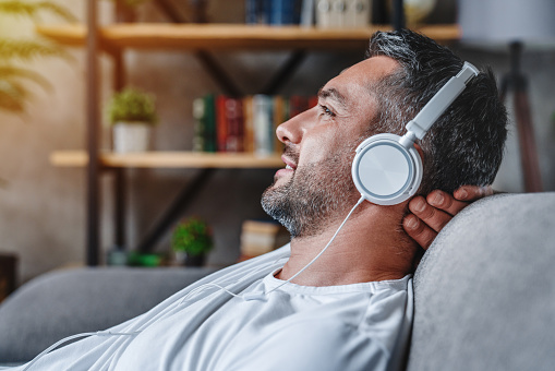 Yound adult man in a long-sleeved white shirt listening to music on white headphones.