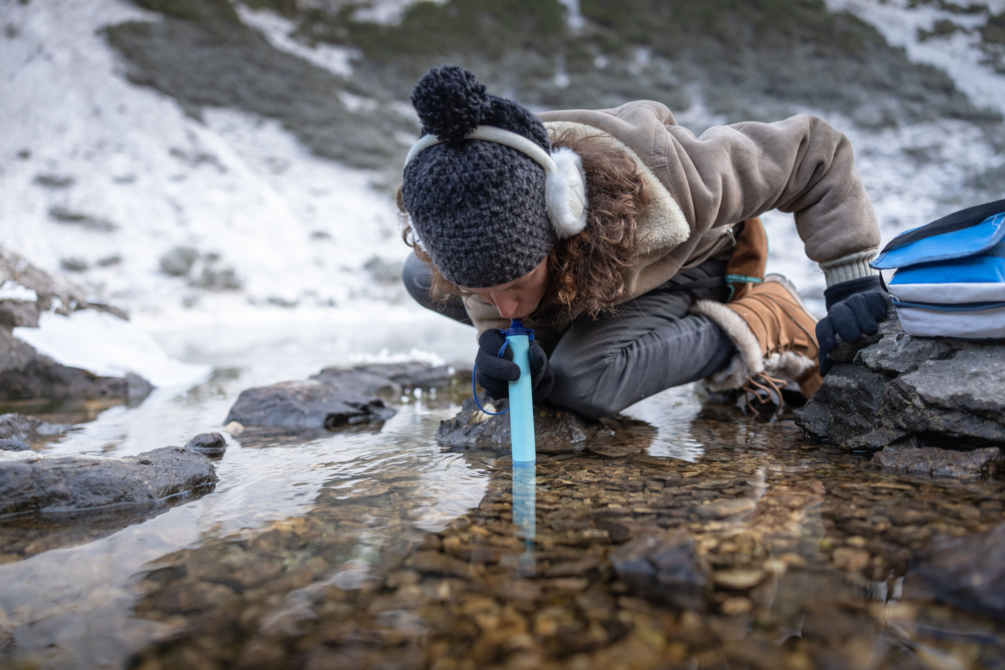 A woman drinking from a live stream using lifestraw