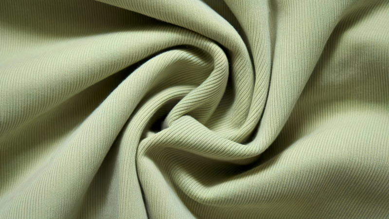 A close-up, top-down view of a rippling swatch of light green recycled polyester fabric.