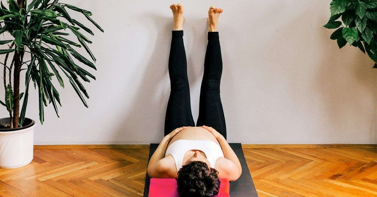 A woman practicing the Legs-Up-the-Wall Pose, which is one of the yoga poses to avoid during pregnancy