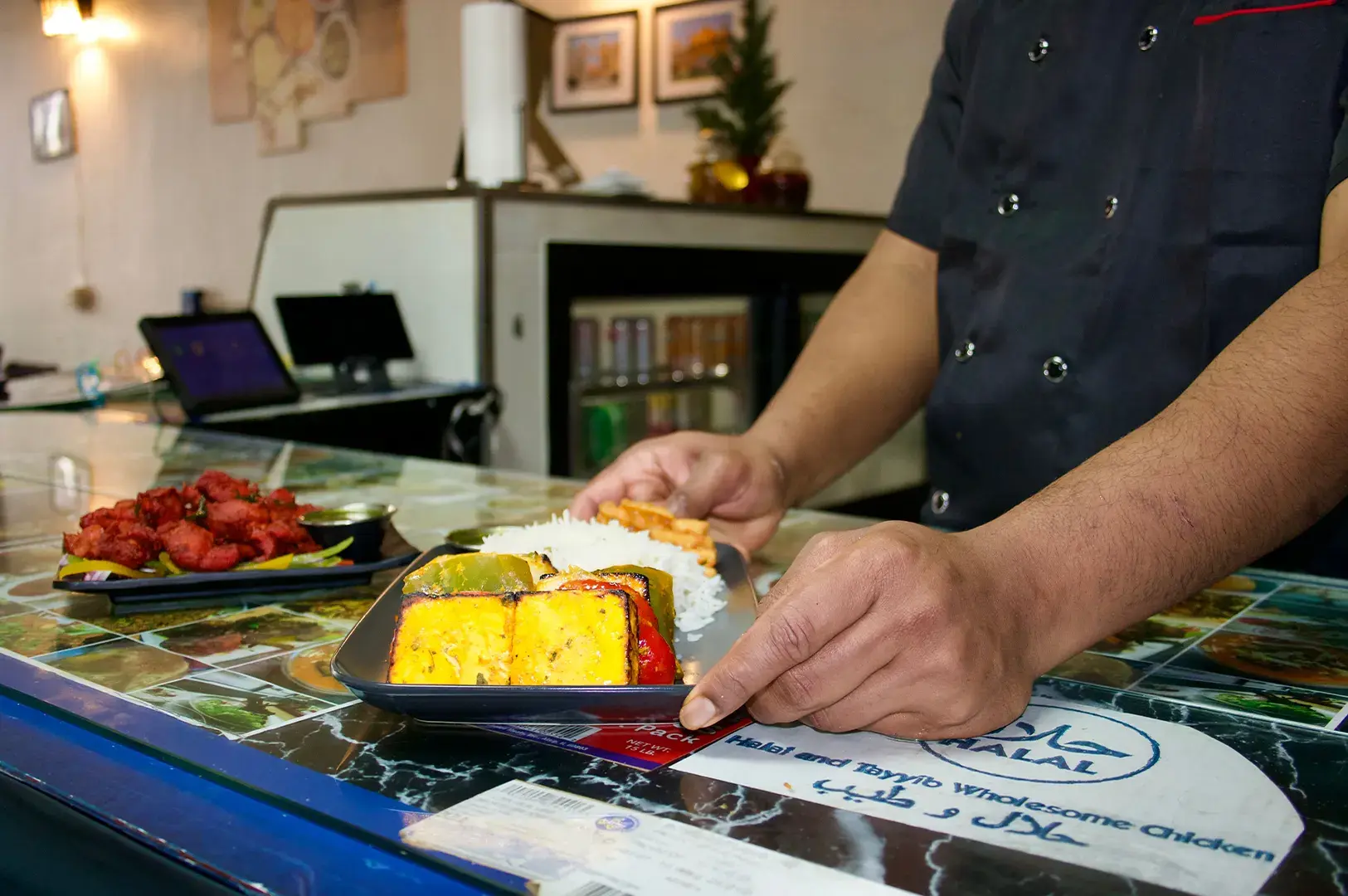 Chef serving a plate of fresh paneer tikka with rice and a side of chicken appetizers at a Halal restaurant.