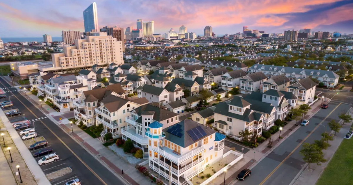 A sunset aerial view of Atlantic City showing rows of beach houses in the foreground with the city skyline and casinos in the distance.