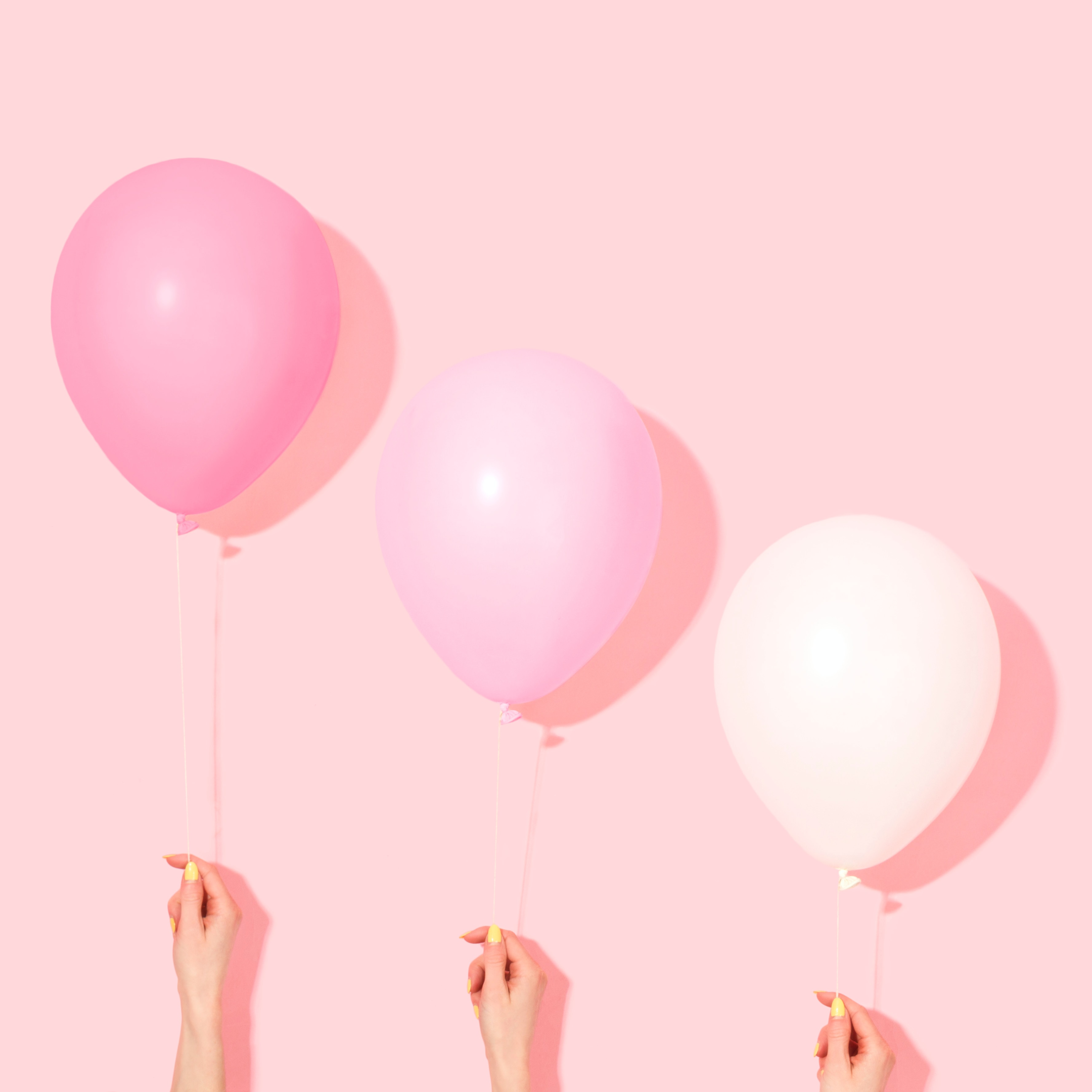 Three pink balloons of different gradients are held up against a pink background.