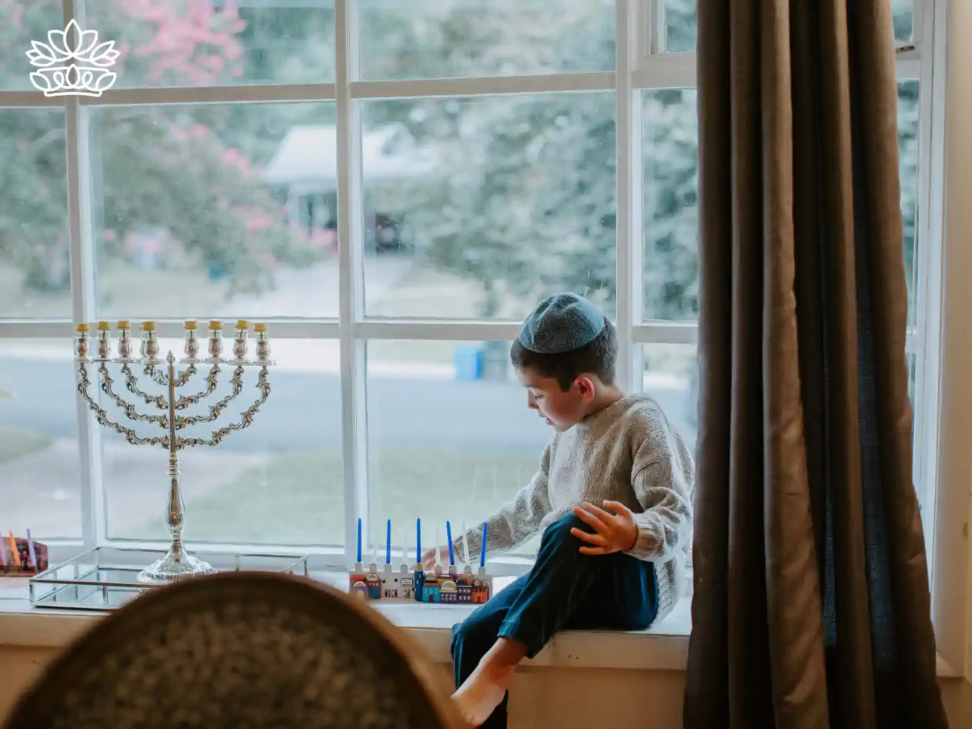 A young boy sitting by a window, gazing at a menorah with lit candles during Hanukkah. Fabulous Flowers and Gifts - Hanukkah Collection.