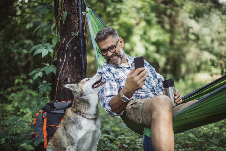 Man sitting in a hammock with his dog. 