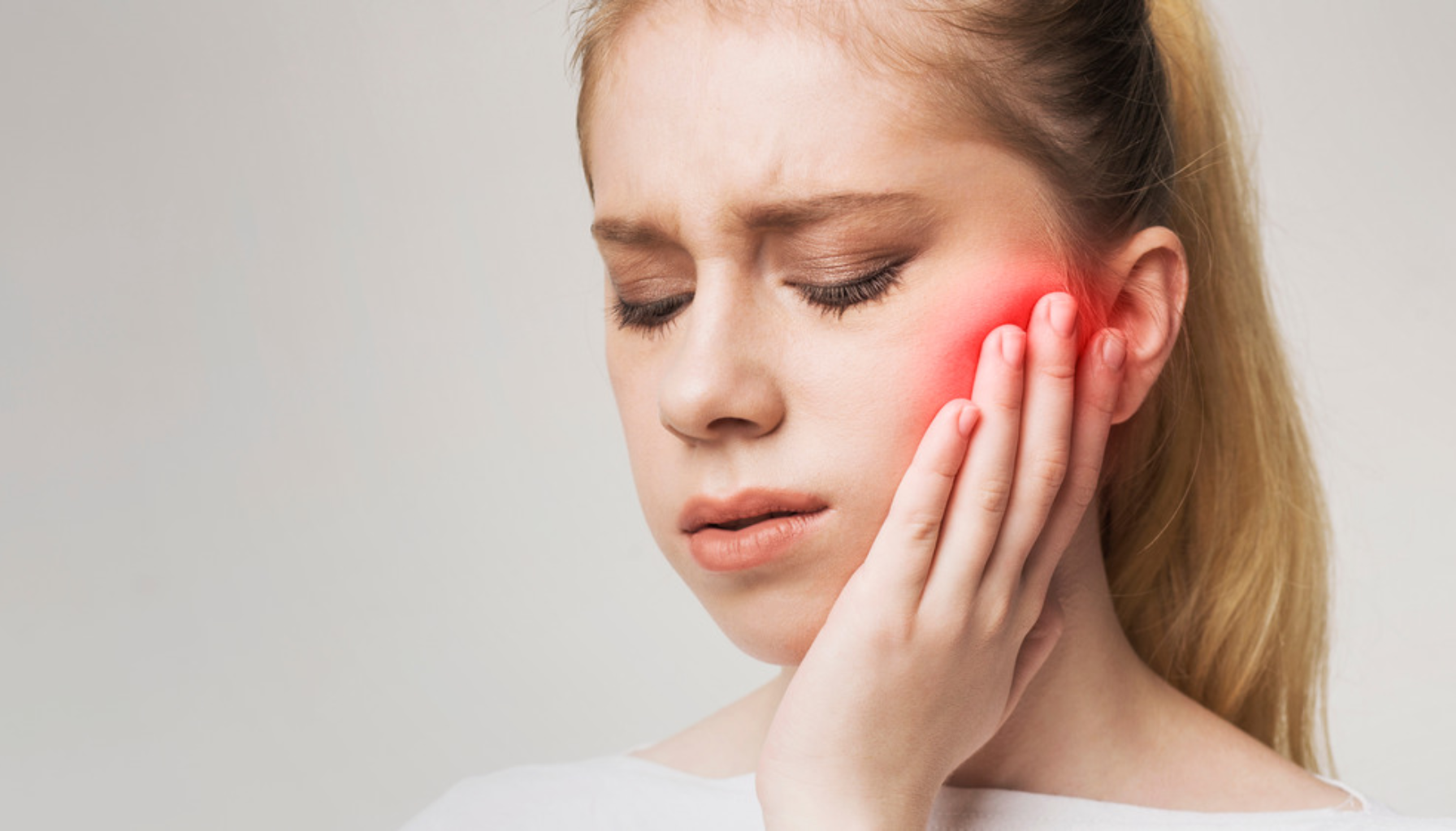 Ung kvinne med øm kjeve holder hånden mot kinnet.