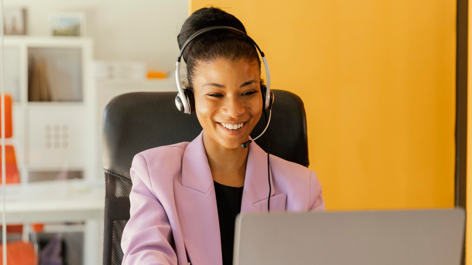A businesswoman wearing a headset answers a voip call in front of a monitor.