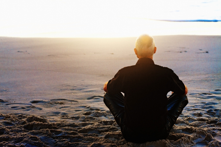 Man meditating on a beach at sunset. 