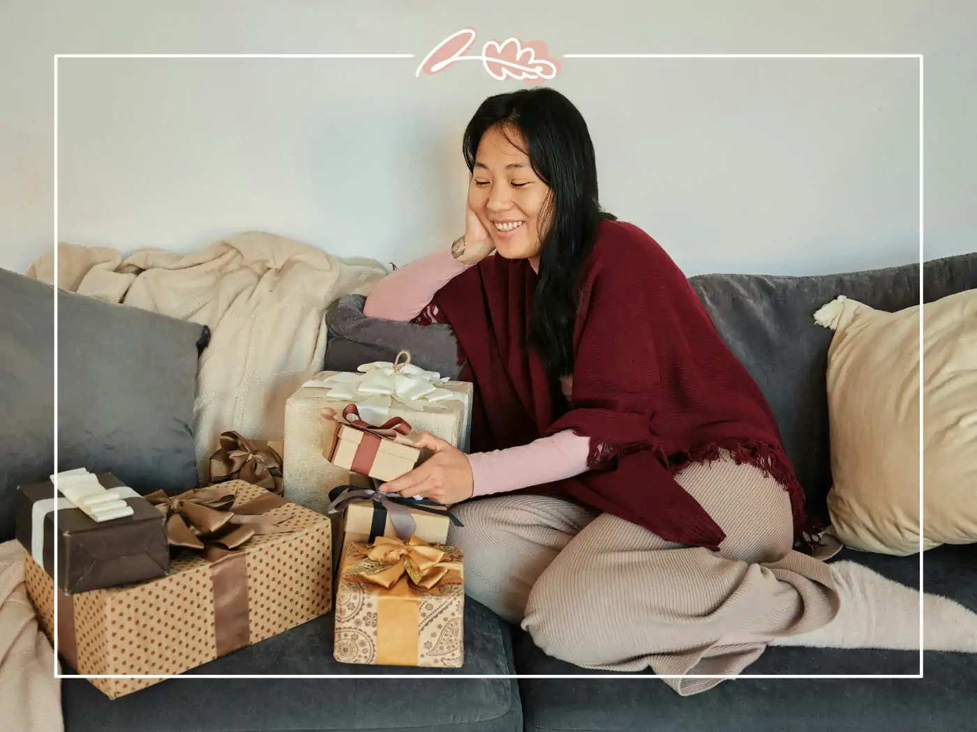 A woman in a red shawl sits on a couch surrounded by beautifully wrapped gifts. Fabulous Flowers and Gifts.